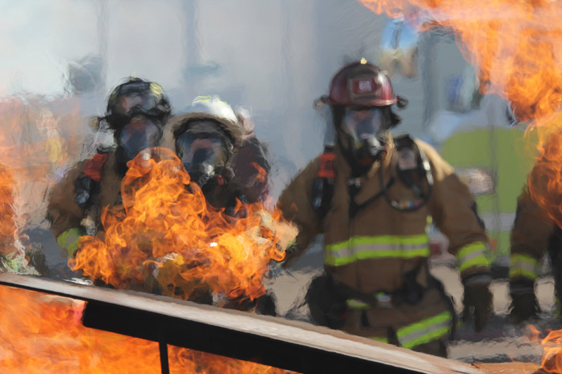 Firefighters wearing their full gear stand behind the flames of training blaze